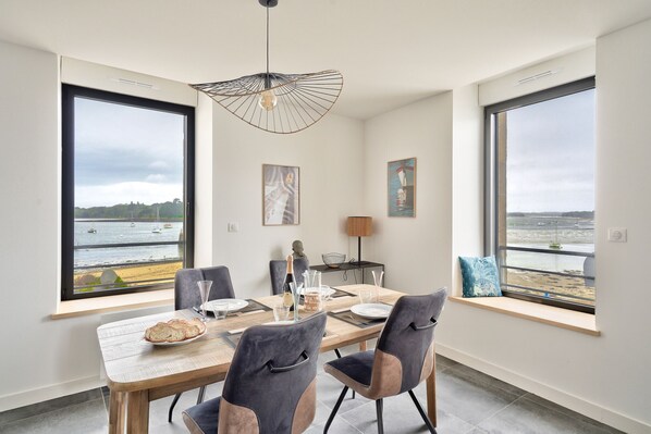 A dining area with a view of the sea, a table set with plates and glasses, and modern chairs. - Beachfront apartment for 4 (Ile Tudy)