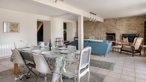 Amplia sala de estar con pared de piedra, chimenea y comedor con una mesa dispuesta para cuatro.