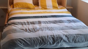 A bed with a wooden frame and a headboard, two pillows, and a striped bedspread. - Cosy studio in a farmhouse  (UBRAYE)