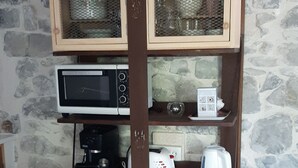 A dining area with a round glass table, two wooden chairs, a wooden cabinet with shelves, a microwave, a toaster, and a coffee maker. - Cosy studio in a farmhouse  (UBRAYE)
