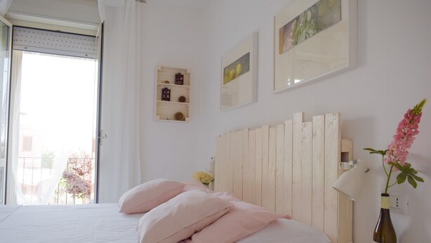 A bedroom with a bed, a bedside table, a lamp, a bottle, and a window with curtains.