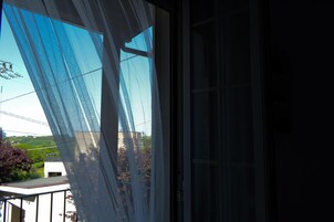 Vista a través de una ventana con mosquitera, un balcón y cielo despejado.