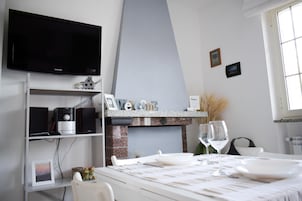 Habitación de hotel moderna con televisión de pantalla plana, chimenea, mesa de comedor para dos personas y vistas al exterior.