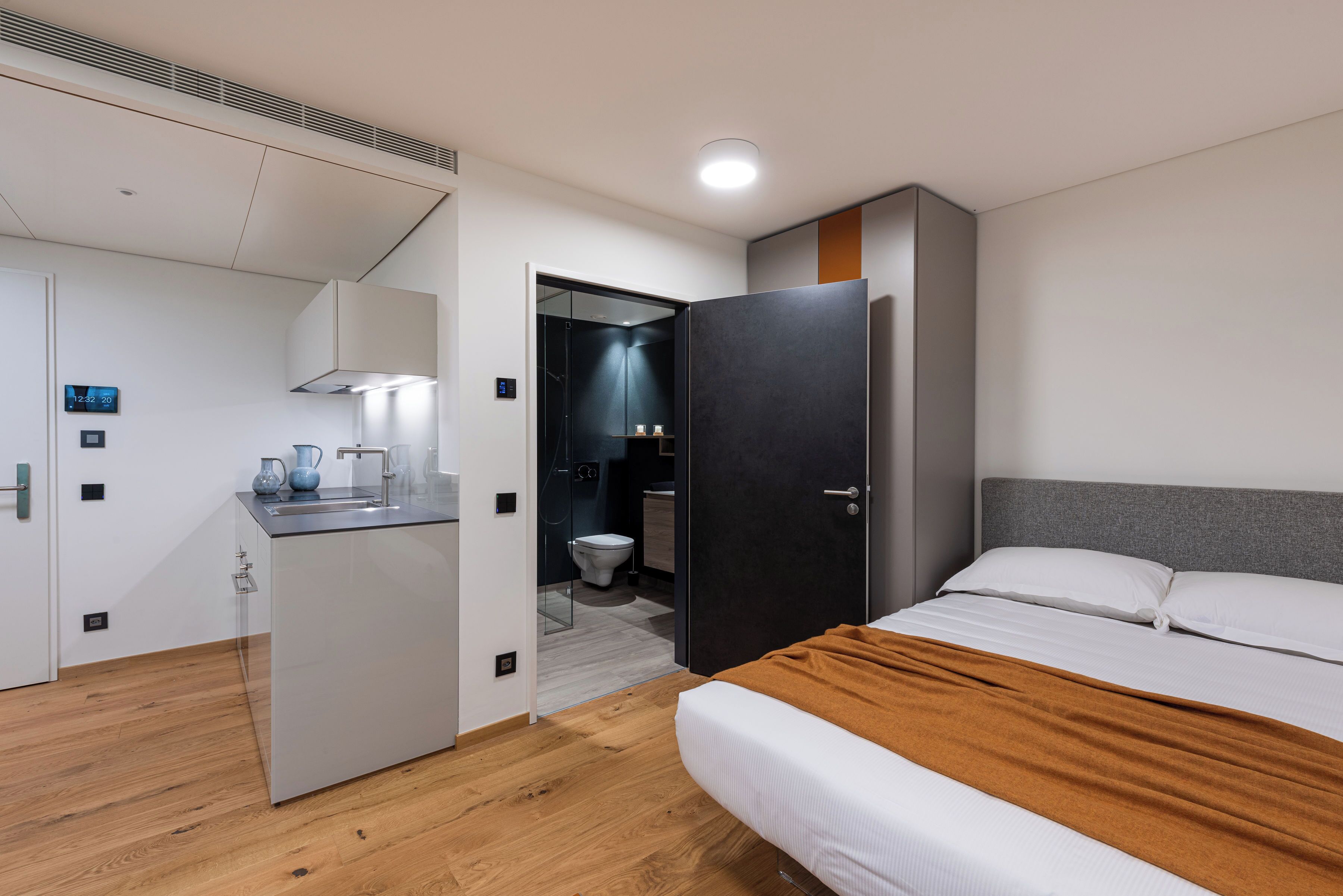 A modern hotel room with a bed, a bathroom, and a kitchenette.