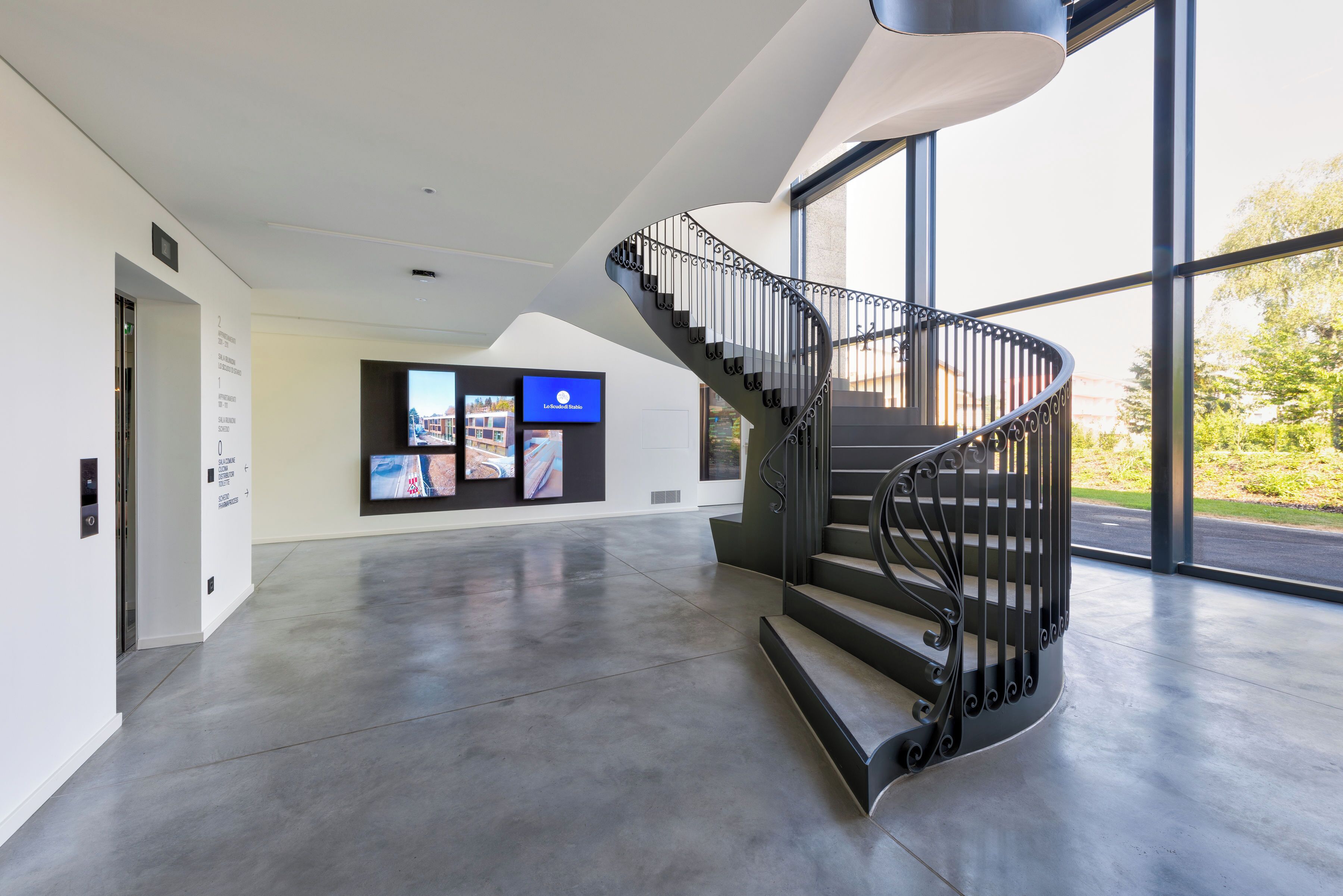 A modern interior with a curved staircase, a digital display wall, and large windows.