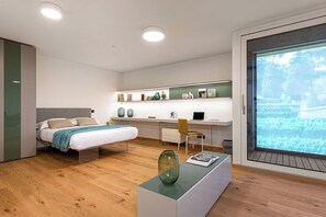 Relax in this serene bedroom with a central bed, desk, and comfortable chair, offering a view of the outdoors.