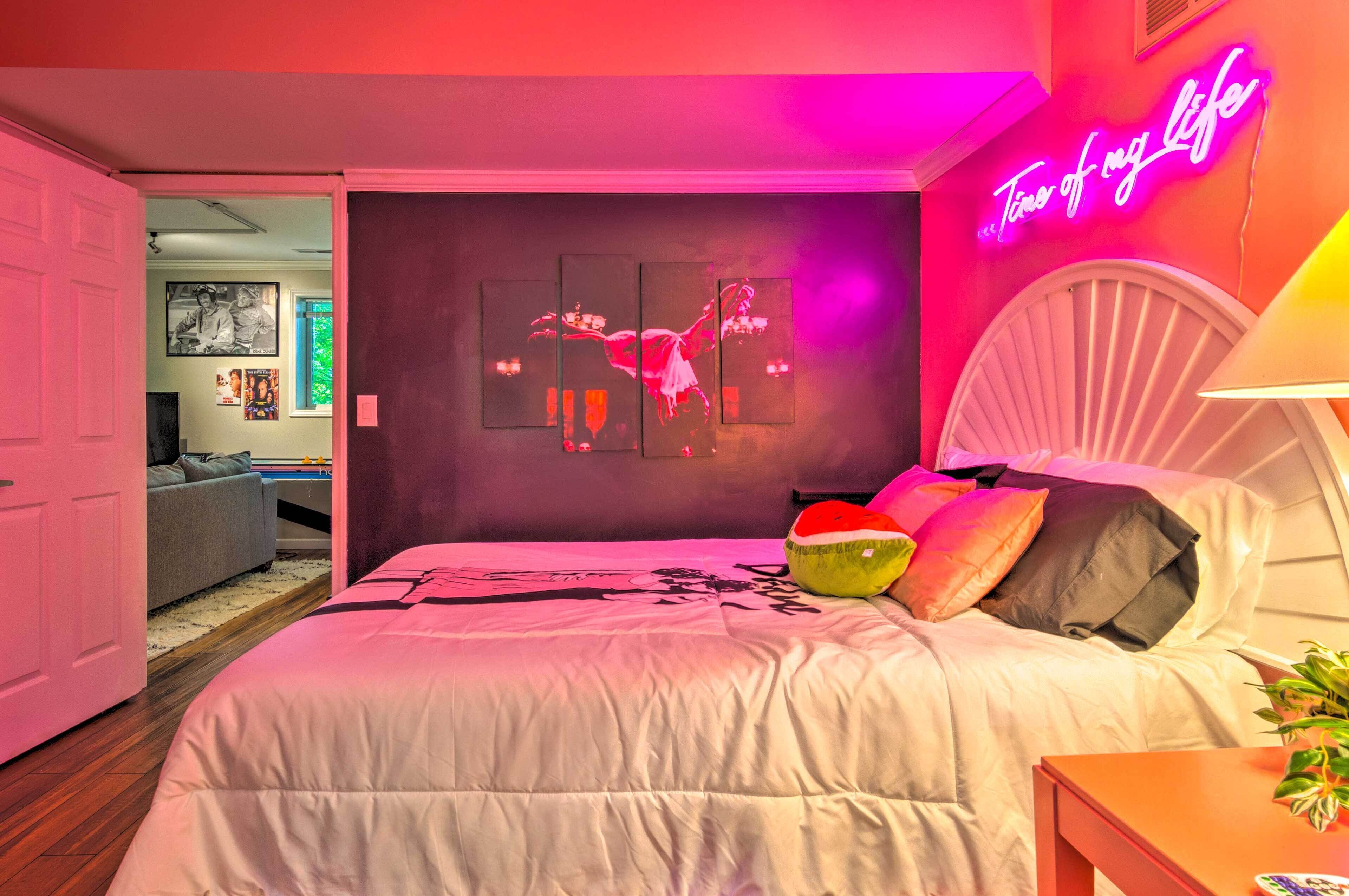 A bedroom with a bed, a neon sign, and a wall art piece.