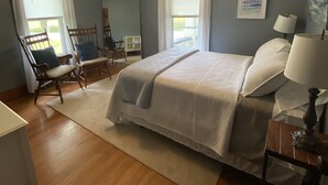 Une chambre à coucher avec un lit, deux chaises, un ventilateur de plafond, une table de chevet et une lampe.