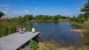 A concrete dock with a chair and a white bucket, overlooking a calm lake surrounded by greenery.