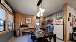 A kitchen with wooden cabinets, a dining table with chairs, a refrigerator, and a hanging light fixture.