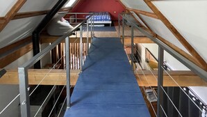 An attic bedroom with a sloped ceiling, wooden beams, a blue carpet, a bed, and a chandelier. - The mountains win you over (Campan)