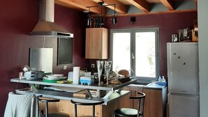 A kitchen with wooden beams, a refrigerator, a stove, and bar stools. - The mountains win you over (Campan)