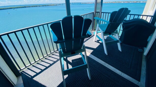 Een balkon met twee Adirondack-stoelen, een uitzicht op een brug en een rustig wateroppervlak.
