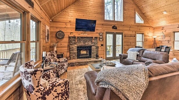 Un intérieur de chalet chaleureux avec une cheminée en pierre, des murs en bois et de grandes fenêtres.