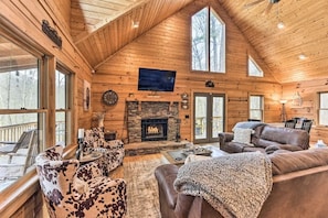 Cozy cabin interior with a stone fireplace, comfortable seating area, and large window.