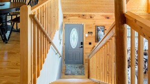 Un intérieur en bois avec un escalier menant à une porte, des rampes d’escalier en bois et un coin repas avec des chaises.