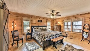 Une chambre dans une cabane en bois, avec un lit, une chaise, un bureau et un ventilateur de plafond.