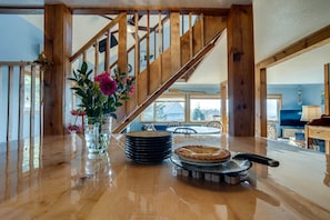 Una escalera de madera con barandilla de vidrio, una mesa de comedor con tarta, un jarrón con flores y una campana.