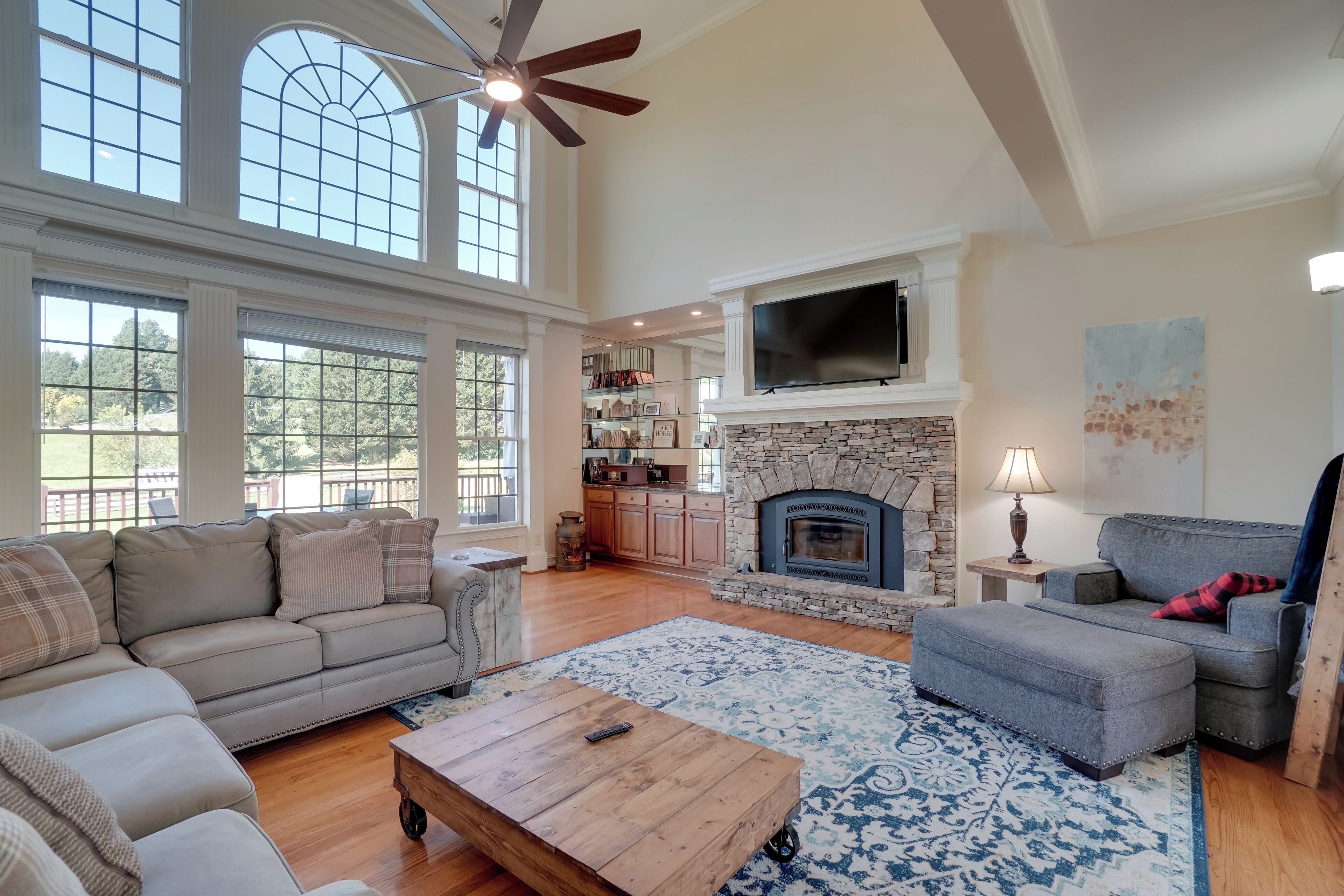A spacious living room with a fireplace, a large window, and a ceiling fan.