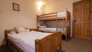Une chambre avec deux lits superposés en bois, un lit simple, une table de chevet, une lampe fixée au mur et une armoire en bois.