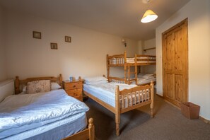 Cozy bedroom with two bunk beds, a single bed, and a nightstand with a lamp, plus a wardrobe and framed pictures on the walls.
