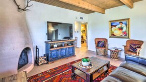 A rustic living room with a fireplace, wooden ceiling beams, a TV, and traditional furniture. - Traditional-Style Adobe Casita - Walk to Dtwn (Santa Fe)