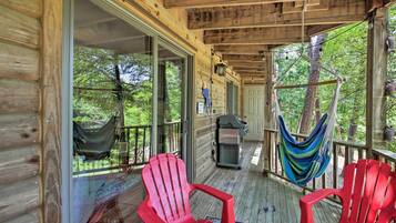 Une véranda en bois avec deux fauteuils Adirondack rouges, un hamac et un barbecue.
