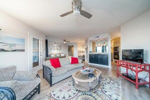 A spacious living room with a sofa, armchairs, a coffee table, and a television.