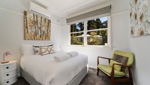 Un dormitorio con cama, ventana con vistas, silla y mesita de noche.
