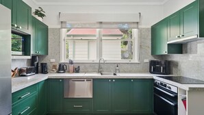 Una cocina moderna con gabinetes verdes, un lavavajillas de acero inoxidable, un horno empotrado y una ventana con vista a una casa.