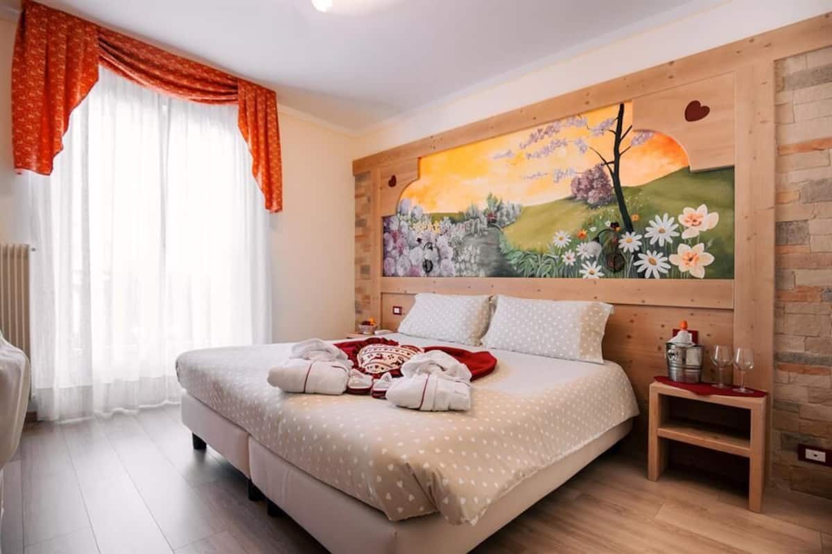 Ein Schlafzimmer mit einem großen Bett, einem Gemälde an der Wand, einem Holz-Kopfteil und einem Nachttisch mit Gläsern und einer Flasche.