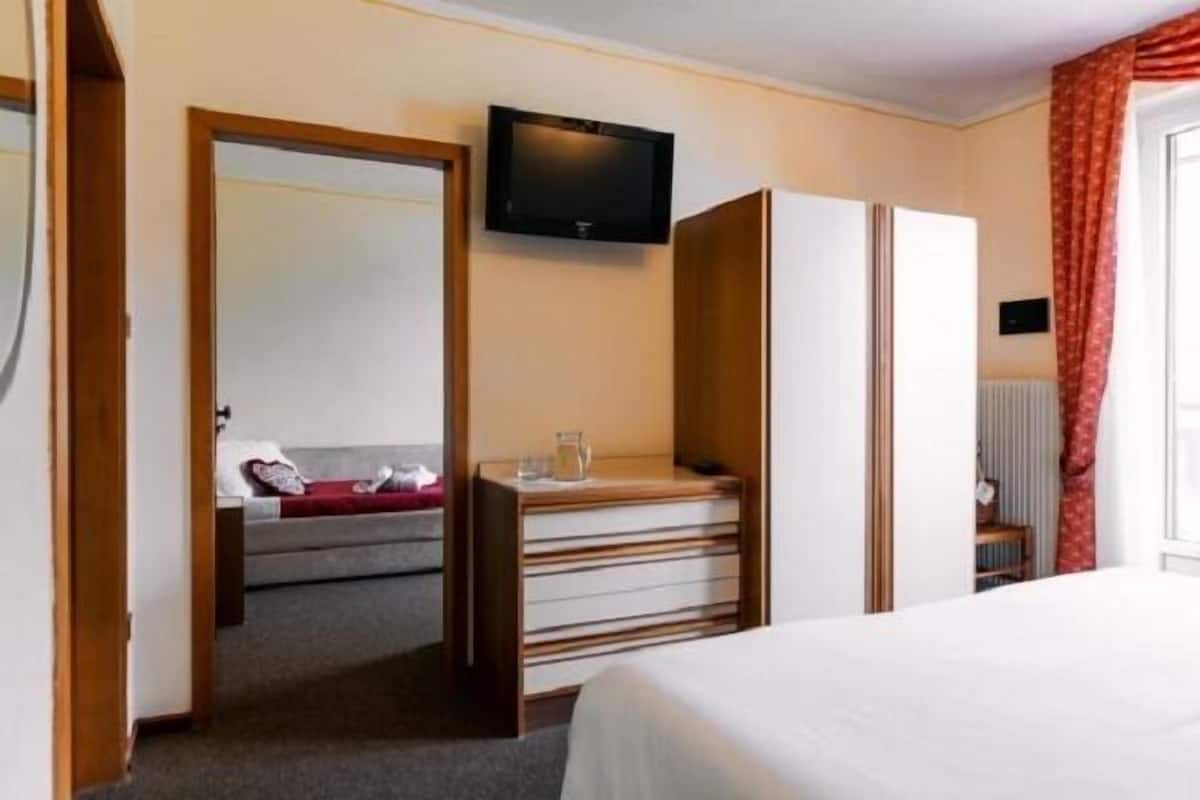 Ein Hotelzimmer mit Bett, Schreibtisch mit Schubladen, einem an der Wand montierten Fernseher und einem Fenster mit Vorhängen.