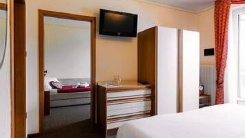 A hotel room with a bed, a desk with drawers, a television mounted on the wall, and a window with curtains.
