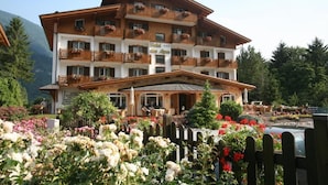 A multi-story hotel with balconies, a covered entrance, and a garden with flowers. - Hotel Des Alpes (Molveno)