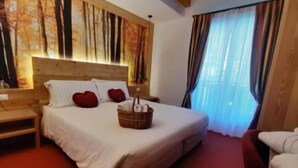 A hotel room with a large bed, a wooden headboard, a bedside table, and a window with curtains. - Hotel Des Alpes (Molveno)