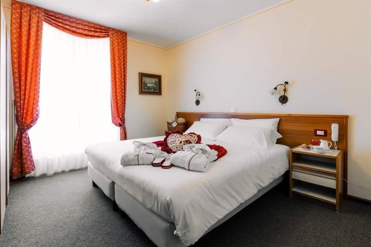 Ein Hotelzimmer mit einem großen Bett, einem Nachttisch mit Lampe und einem Fenster mit Vorhängen.