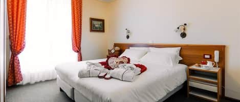 A hotel room with a large bed, a bedside table with a lamp, and a window with curtains.