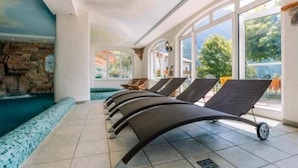 A pool area with lounge chairs and a stone wall. - Hotel Des Alpes (Molveno)