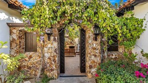 A stone archway with climbing plants, leading to a courtyard with a bench and a wooden table. - Ultra Private Villa w/ Open Floor Plan, Premium Bedding, & Big Ocean View. Daily Butler Included (San Jose del Cabo)