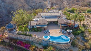 A large villa with a swimming pool, multiple outdoor seating areas, and a stone retaining wall. - Ultra Private Villa w/ Open Floor Plan, Premium Bedding, & Big Ocean View. Daily Butler Included (San Jose del Cabo)