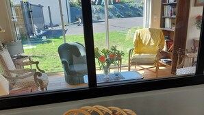 Uma cesta de vime com frutas sobre uma mesa, uma janela com vista para um jardim e uma estante de livros.