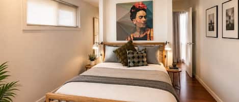 A bedroom with a bed, bedside tables, a painting, and a window.