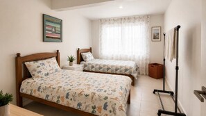 A bedroom with two beds, a standing lamp, and a window with curtains.