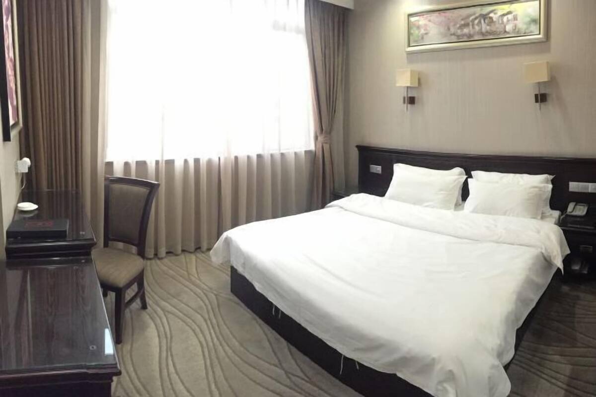 Quarto de hotel com uma cama grande, uma escrivaninha, uma cadeira e um quadro na parede.
