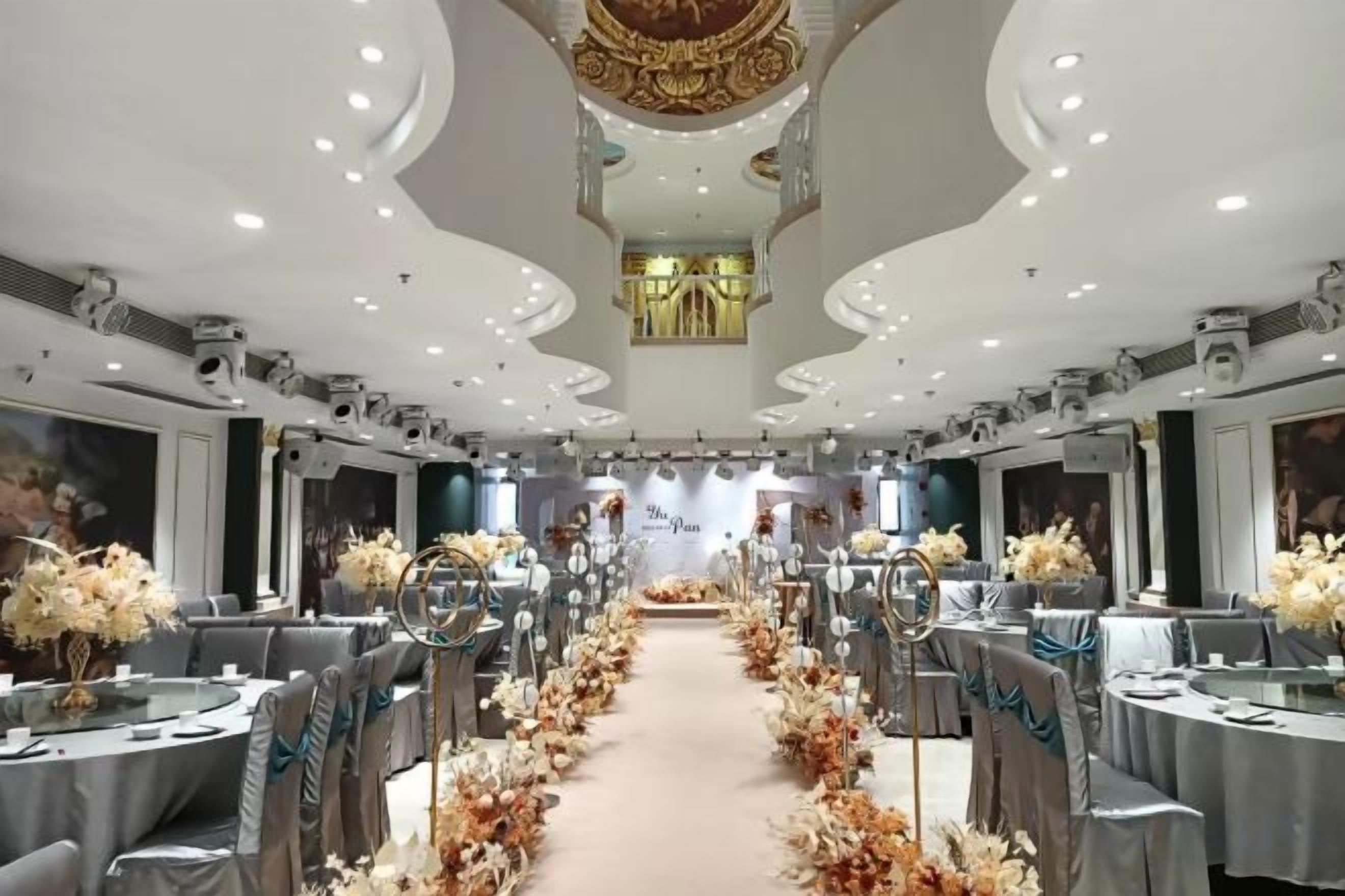 A banquet hall with round tables, floral centerpieces, and a central aisle.