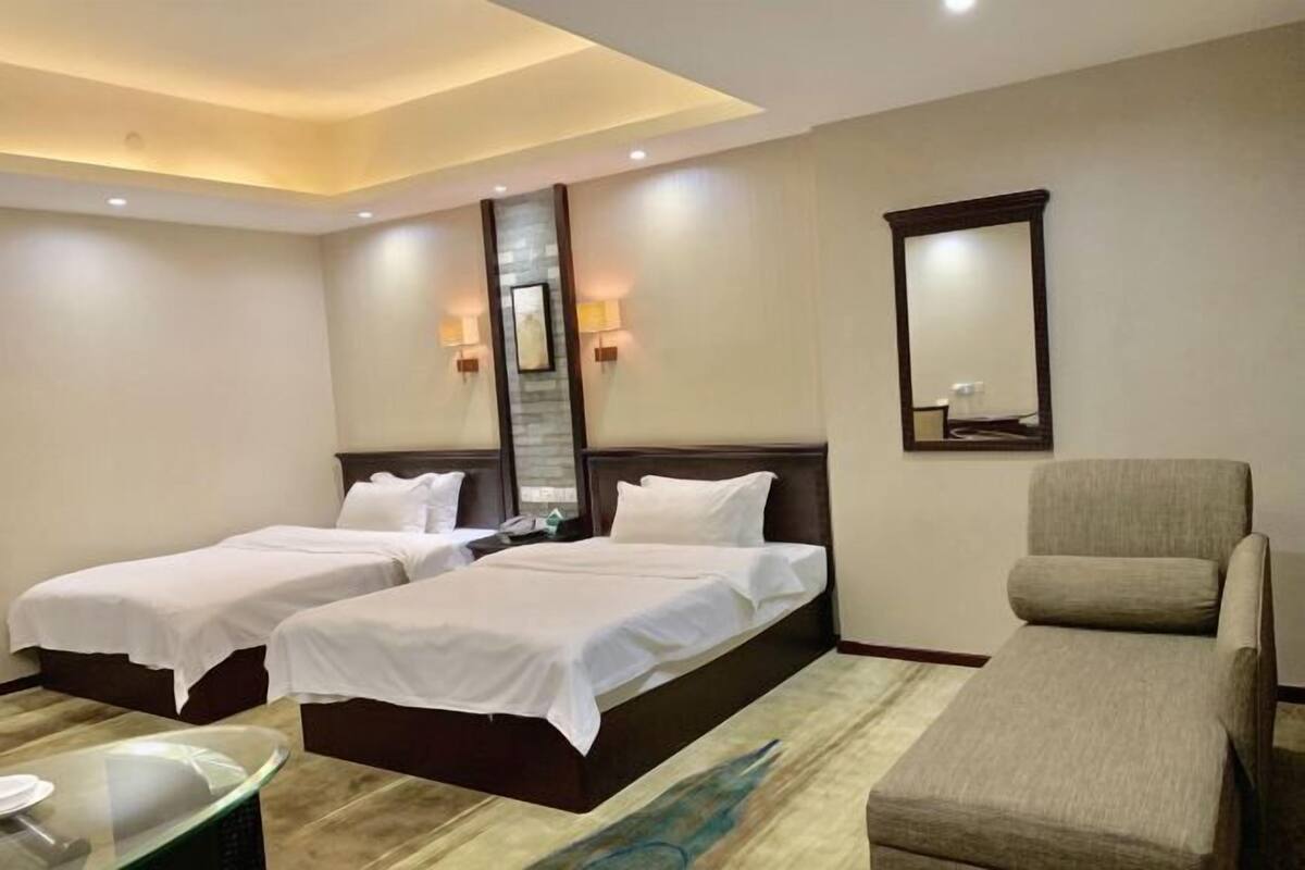 Quarto de hotel com duas camas, uma cadeira, uma mesa de vidro e um espelho.