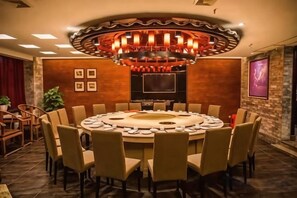 A conference room with a round table, chairs, a large chandelier, a flat-screen TV, and a stone wall. - Hengsheng Kejia Courtyard (Xinfeng)