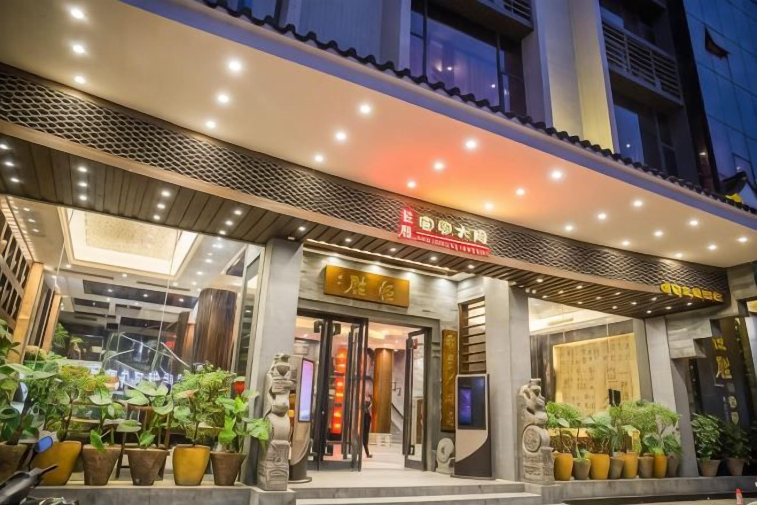 A hotel entrance with a modern design, featuring a prominent entrance, potted plants, and illuminated signage.