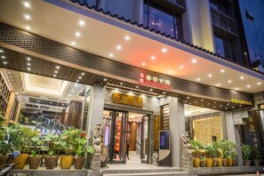 A hotel entrance with a modern design, featuring a prominent entrance, potted plants, and illuminated signage. - Hengsheng Kejia Courtyard (Xinfeng)