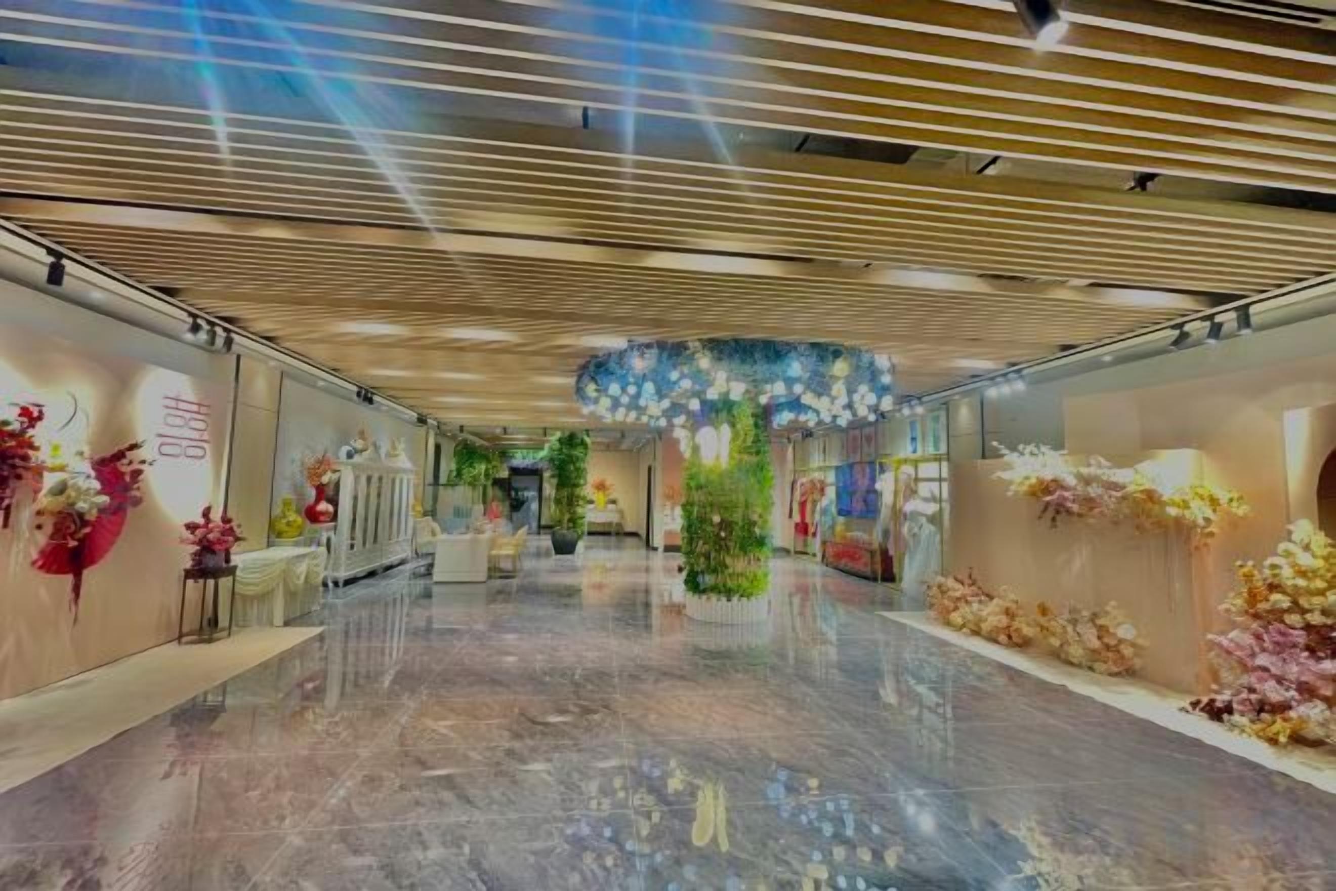 A spacious corridor with a polished floor, decorative floral arrangements, and a modern ceiling design.